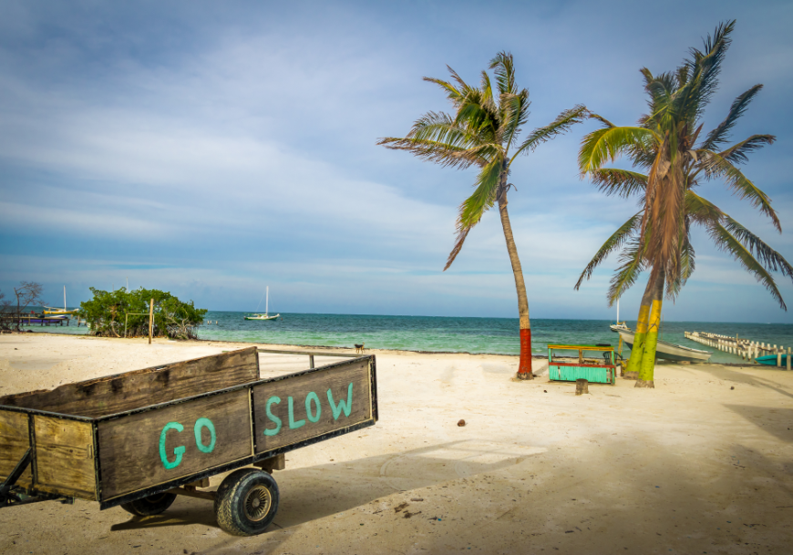 There's nothing fast or fancy about life in Belize, and for you, that might be PERFECT! Moving to Belize Image: A wooden cart on a beach has "Go Slow" written on it.