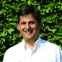 Anywhere Ecuador's charismatic and knowledgable Percy Coll-Santillan. Mr. Coll-Santillan Smiles whilst wearing a white button-down in front of a leafy green background.