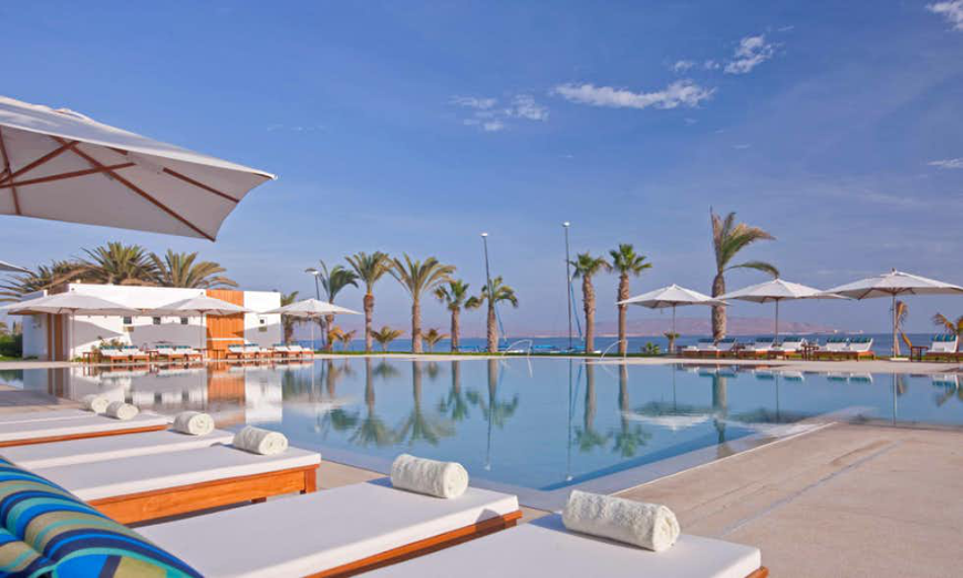 Most Romantic Hotels in Peru Image: Pristine pool, palm trees, white lounge chairs, and umbrellas at Hotel Paracas.