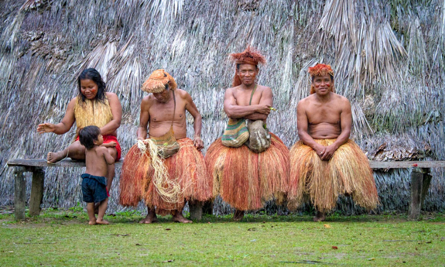 Experience a new culture off the page. Sustainable Travel In Peru Image: One female member and child, and three male members of the Yagua Tribe sit on a bench.