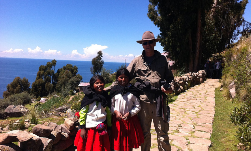 Get to know people around the world, not just within the walls of a resort. Sustainable Travel In Peru Image: A man in khakis poses with two young Peruvian women wearing red skirts, white blouses, and black wraps.