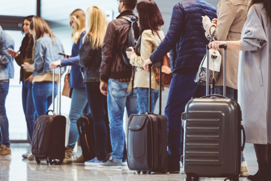 Think a crowded airport is annoying? Imagine feeling crowded in your own home country. Sustainable Travel Image: A line of travelers is queued in an airport with their luggage.