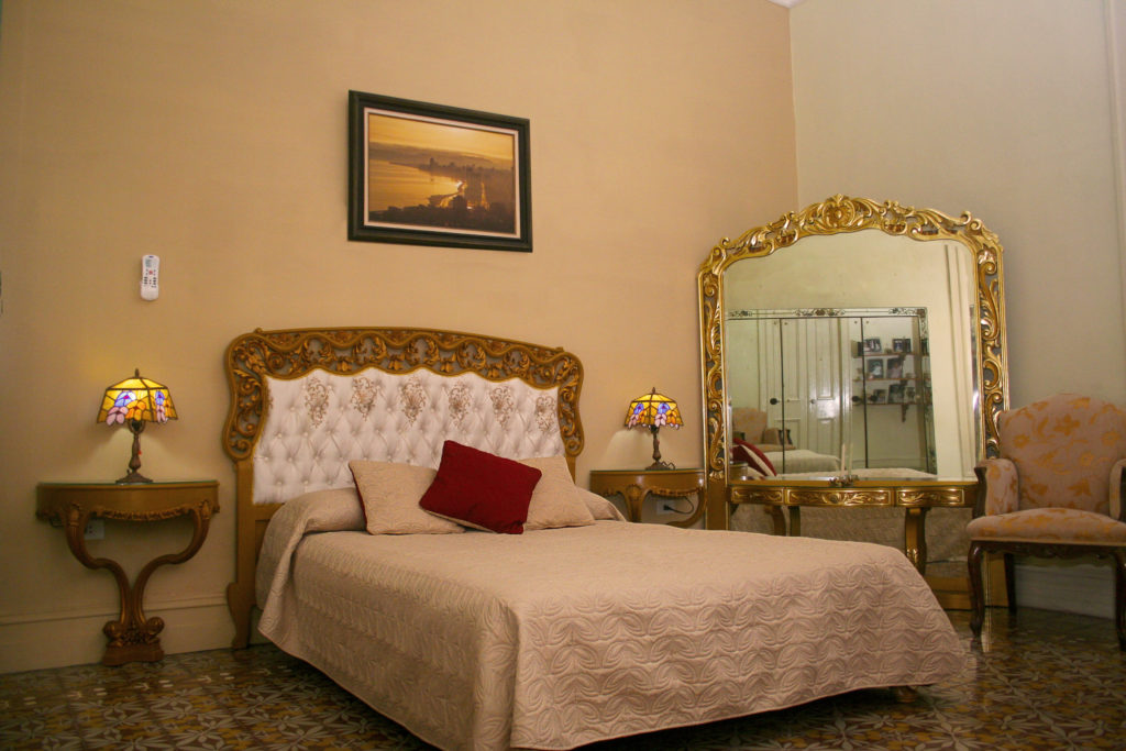 Unlike a traditional hotel or resort, a casa particular is guaranteed to be a unique experience. Legally Travel To Cuba Image: A simpe but well decorated room in the Hostal del Angel includes a large bed, two nightstands with lamps. an oversized mirror, and chair.