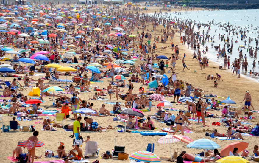 Chances are, you aren't the only one who thought of heading somewhere warm to escape the chilly months. Tropical Holiday Image: A crowded beach full of other tropical holiday revelers with their sun umbrellas, beach towels, and toys all over the beach and in the water.