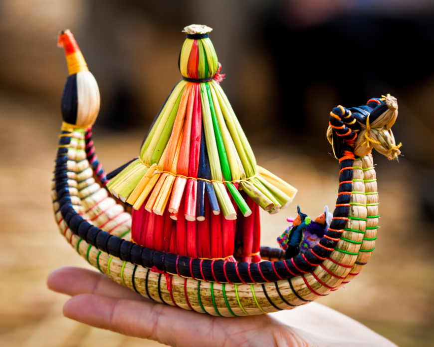 Support indigenous artisans and sustainable souvenirs! Peru Souvenir Image: A person (not shown) holds a small colourful reed boat—a Peruvian souvenir from Uros island—in the palm of their hand.