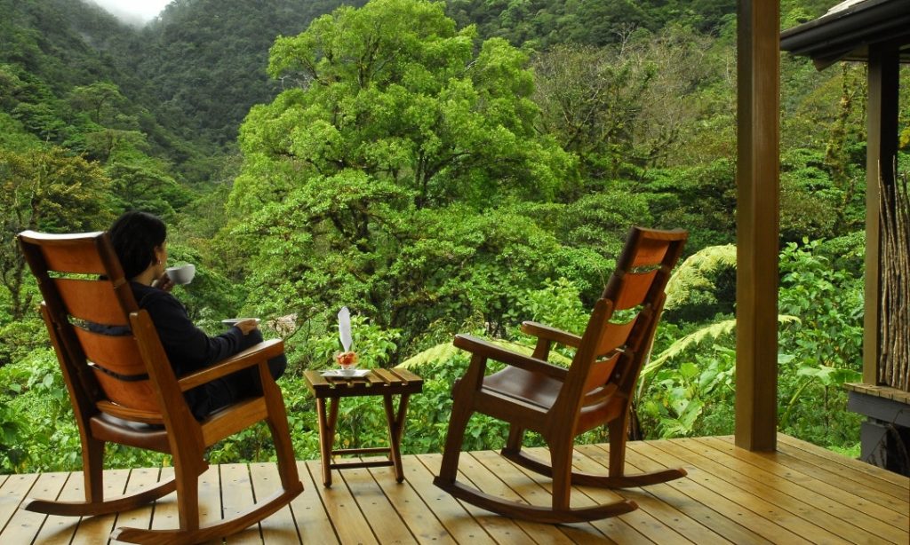 Imagine waking up to this on the first morning of your honeymoon or anniversary... Unique Honeymoon Image: A woman sits in one of tea rocking chairs, sipping tea whilst quietly looking out at a lush green tropical forest.