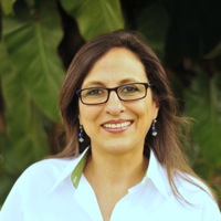 The lovely and dedicated manager of our Belize operations, Bitty Ramirez-Portilla--she is a brunette wearing black-framed glasses, dangling earrings, and a dress shirt.