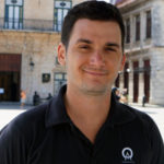 The dashing manager of Anywhere Cuba, José Miguel. Smiles softly whilst wearing a black polo shirt which matches his black hair.