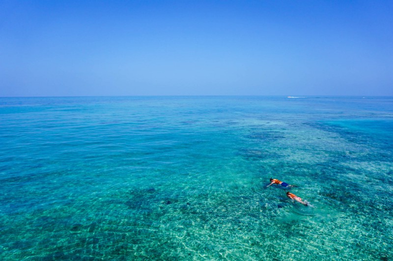 Life's a beach when you spend every day of your vacation in Belize. What To Pack Image: An aerial shot of two people snorkeling in crystal clear turquoise colored water.