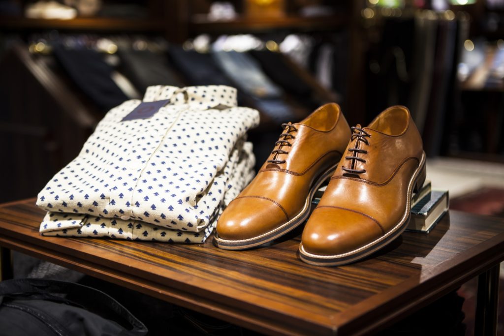 Keep it classy ;-) What To Pack Image: Polished light brown dress shoes, and a light-colored and patterned business casual buttonw-down dress shirt sit on a wooden table with books.